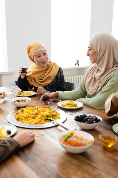 asian muslim woman holding glass of tea near arabian daughter during family dinner - Fotoğraf, Görsel