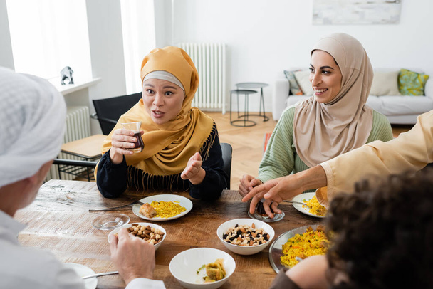 азіатська жінка вказує рукою під час розмови біля усміхненої мусульманської дочки і розмитої сім'ї
 - Фото, зображення