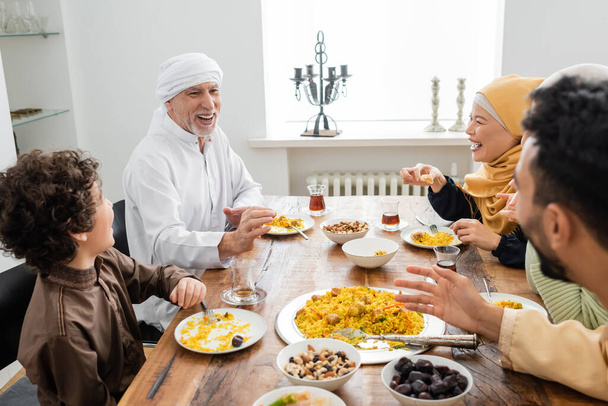 happy middle aged muslim man talking to interracial family during dinner at home - Foto, afbeelding