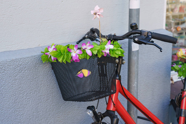 Polkupyörän ohjaustankoon kiinnitetty kori on koristeltu kukilla. Sulje se.. - Valokuva, kuva