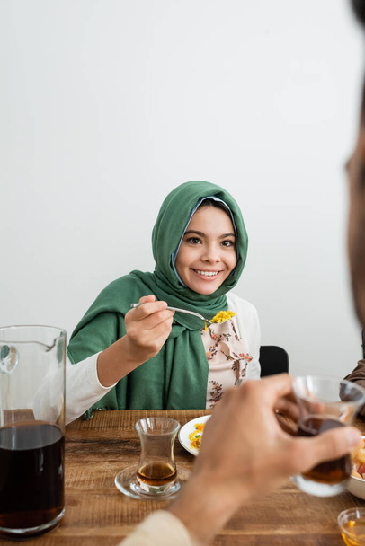 happy muslim girl in hijab eating pilaf near blurred father - Photo, Image