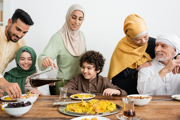 arabská žena nalévání čaje v blízkosti šťastný multietnické muslimské rodiny s večeří doma - Fotografie, Obrázek