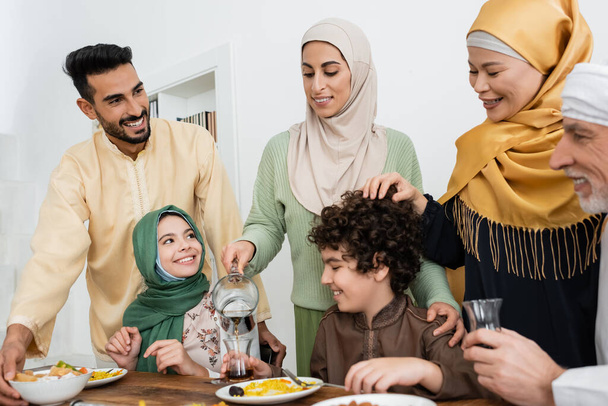 joyful arabian woman poring tea during dinner with interracial muslim family - Photo, image