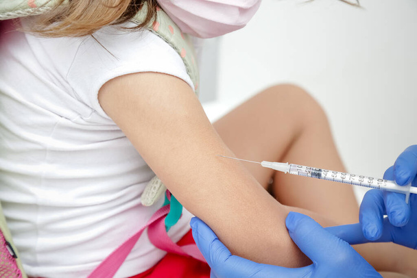 Niño vacunado contra covid 19 vuelve a la escuela de medicina con guante azul y jeringa. - Foto, Imagen