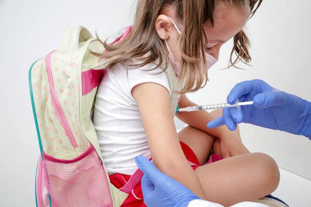Kind wird mit blauem Handschuh und Spritze gegen Covid 19 geimpft. - Foto, Bild