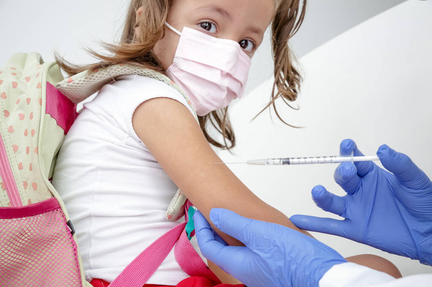 Kind wird mit blauem Handschuh und Spritze gegen Covid 19 geimpft. - Foto, Bild
