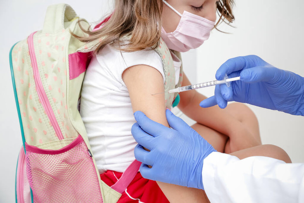 Kind gevaccineerd tegen covid 19 gaat terug naar de medische school met blauwe handschoen en spuit. - Foto, afbeelding