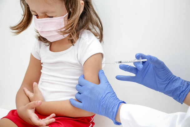 Child being vaccinated against covid 19 goes back to medical school with blue glove and syringe. - Photo, Image