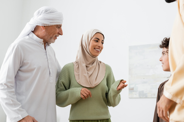 gelukkig moslim vrouw wijzend naar Arabische zoon in de buurt van volwassen vader en echtgenoot - Foto, afbeelding