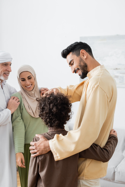 arabský otec a syn objímající v blízkosti šťastné mezirasové muslimské rodiny - Fotografie, Obrázek