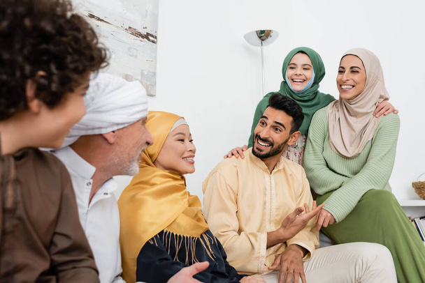 улыбающийся арабский мужчина указывает рукой, разговаривая с веселой многонациональной мусульманской семьей  - Фото, изображение
