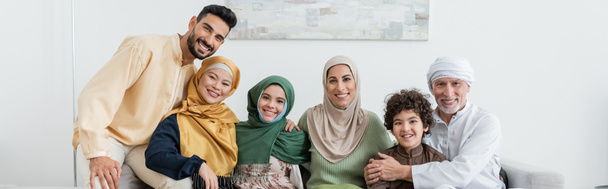 wesoła wielokulturowa muzułmańska rodzina patrząca przed kamerą w domu, baner - Zdjęcie, obraz