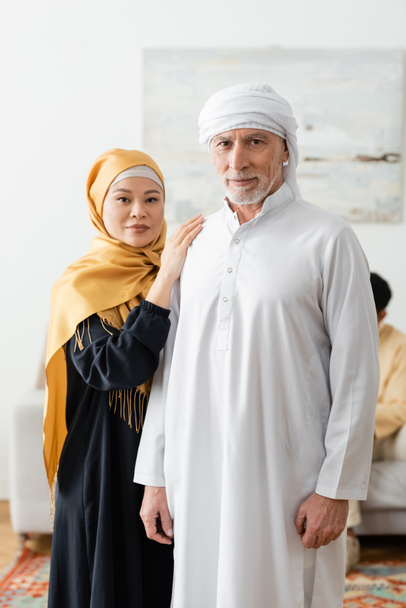 межрасовая пара средних лет в традиционной мусульманской одежде, смотрящая в камеру - Фото, изображение