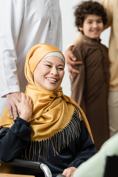 muslimische Asiatin im Hidschab lächelt neben Ehemann und verschwommenem arabischen Enkel - Foto, Bild