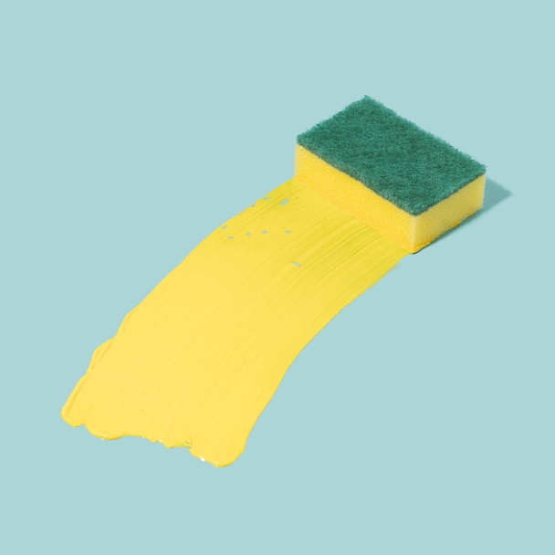 Очищення губки за допомогою жовтої акрилової фарби на пастельно-блакитному тлі. Концепція сюрреалістичного очищення
. - Фото, зображення