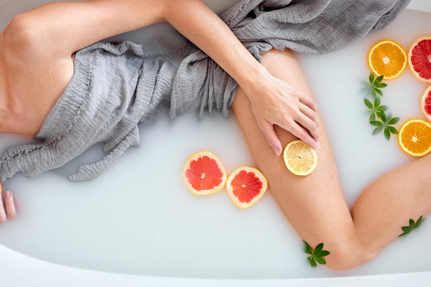 top view on female legs, lady is lying in milk bath with citrus fruits, cropped photo - Fotó, kép