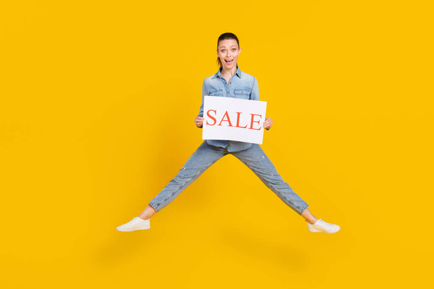 Full length body size photo smiling girl jumping up keeping sale table overjoyed isolated vivid yellow color background - Foto, imagen