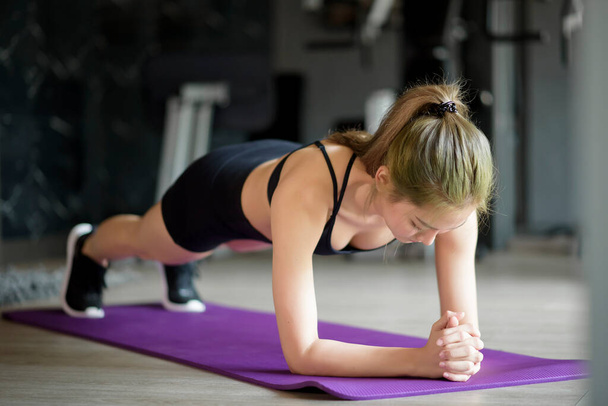A happy beautiful woman is doing yoga plank on mat at the gym, concept of healthy lifestyle, sports, training, wellness, and sport.  - Foto, Imagem