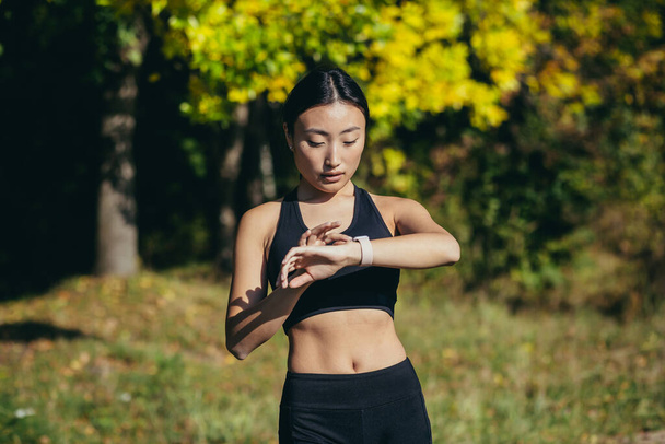 Sporty asian woman looking smart watch at modern track runner using use smartwatch fitness bracelet Portrait fitness female athlete checking result jogging in sportswear in urban city park outdoor - Foto, Imagen