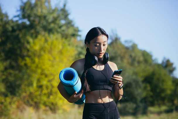 Beautiful asian woman athlete goes to fitness class, listens to music on headphones and uses the phone - Foto, afbeelding