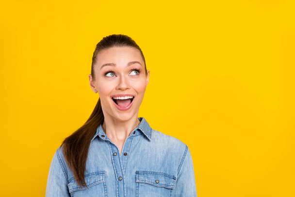 Photo of shocked funky young lady dressed jeans shirt open mouth looking empty space smiling isolated yellow color background - Zdjęcie, obraz