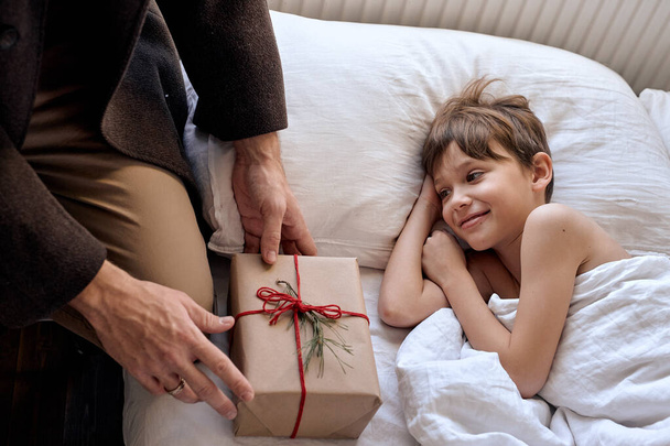 Christmas surprise for beloved son. Kid boy receiving wrapped gift box from father - Fotografie, Obrázek