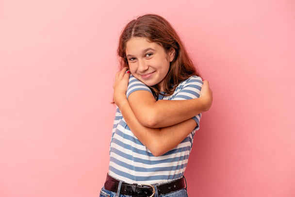 Klein blank meisje geïsoleerd op roze achtergrond knuffels, glimlachend zorgeloos en gelukkig. - Foto, afbeelding
