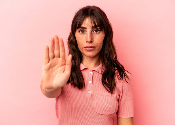 Mujer argentina joven aislada sobre fondo rosa de pie con la mano extendida mostrando señal de stop, previniéndote. - Foto, Imagen