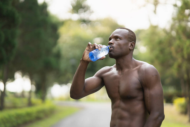 Aantrekkelijke Afrikaanse sportman moe en dorstig na het lopen workout drinkwater. Sport man concept - Foto, afbeelding