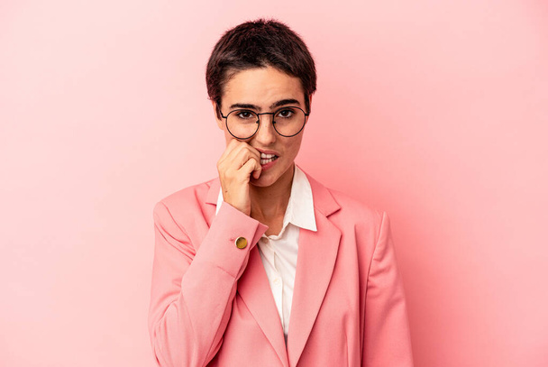 Joven mujer de negocios con una chaqueta rosa aislada sobre fondo rosa mordiendo las uñas, nerviosa y muy ansiosa. - Foto, imagen