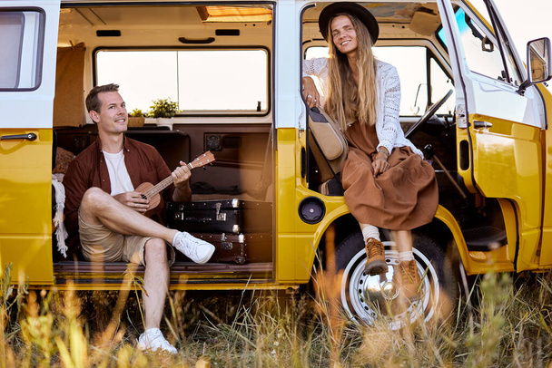 Young hipster couple sitting in camper van playing ukulele, making music together - Foto, Imagem