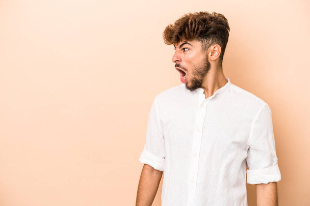 Young arab man isolated on beige background shouting very angry, rage concept, frustrated. - Photo, image