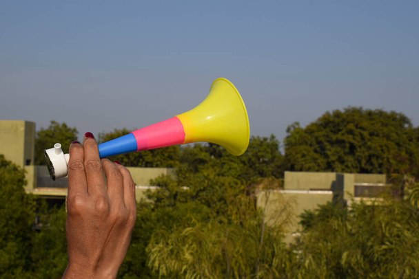 Persona que sostiene el silbato en forma de trompeta que toca el cuerno conocido como Pipudi o pipudo in gujarati. Soplado durante el festival de cometas de Uttarayan o Makar sankranti en la India. Juguete de música divertido utilizado mientras vuela cometa - Foto, imagen