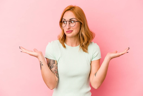 Young caucasian woman isolated on pink background confused and doubtful shrugging shoulders to hold a copy space. - Photo, Image