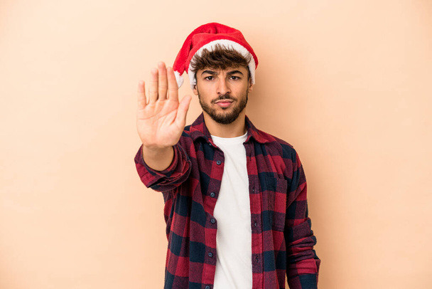 Young arab man celebrating Christmas isolated on beige background standing with outstretched hand showing stop sign, preventing you. - Fotografie, Obrázek