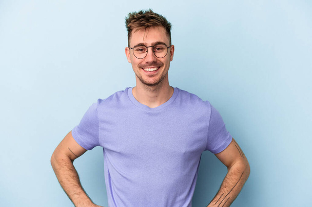 Young caucasian man isolated on blue background confident keeping hands on hips. - Photo, Image