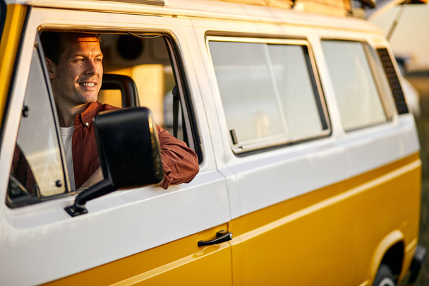 smiling happy man on road trip driving yellow van. Smiling male travelling by van - Photo, image
