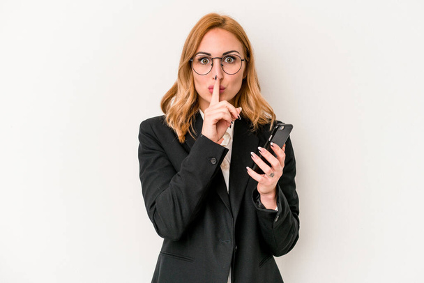 Young business caucasian woman holding mobile phone isolated on white background keeping a secret or asking for silence. - Photo, Image