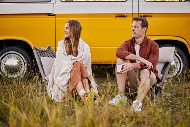 Young caucasian couple sit outdoors next to old vintage van looking at side, relaxed - Φωτογραφία, εικόνα