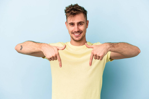 Young caucasian man isolated on blue background points down with fingers, positive feeling. - Photo, Image