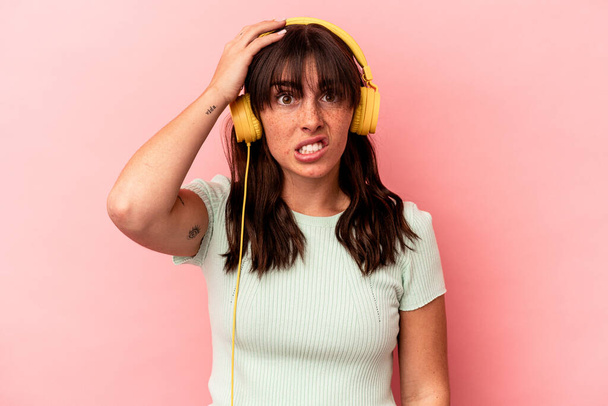 Jonge Argentijnse vrouw luisteren naar muziek geïsoleerd op roze achtergrond wordt geschokt, ze heeft onthouden belangrijke ontmoeting. - Foto, afbeelding