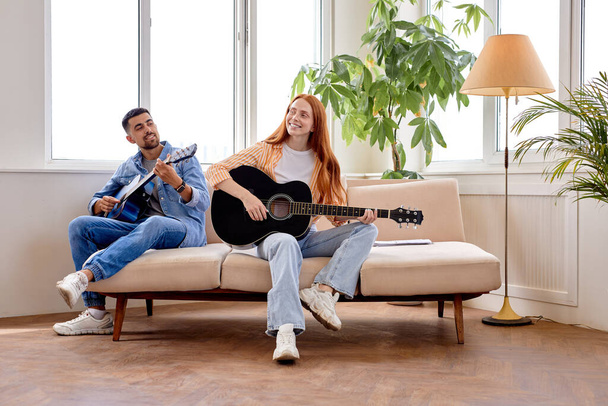 Couple hold guitar and laugh sitting together in living room. Rest time, music concept - Foto, afbeelding
