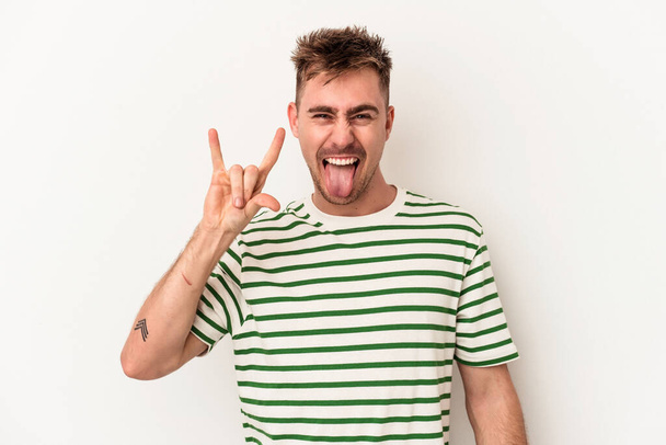 Young caucasian man isolated on white background showing a horns gesture as a revolution concept. - Photo, Image