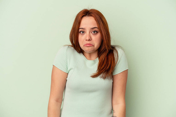 Young caucasian woman isolated on green background shrugs shoulders and open eyes confused. - Photo, Image
