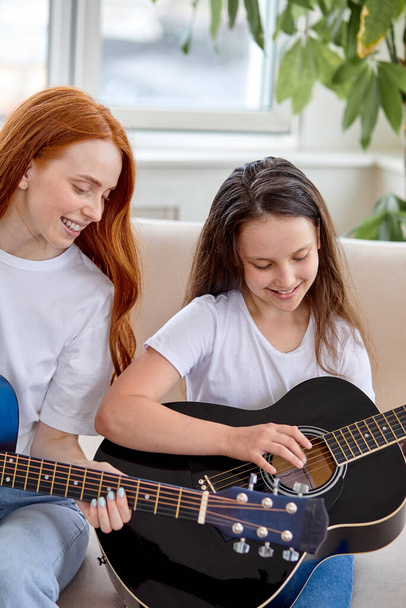 Caucasian woman and little child at home family time sitting on sofa playing guitar - Foto, Bild