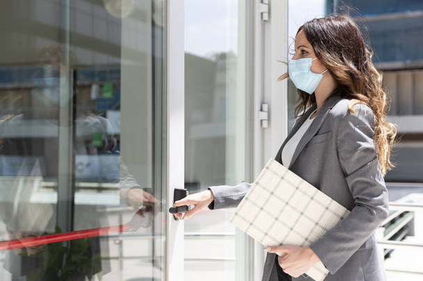 Elegant young Caucasian businesswoman entering her workplace. She is wearing a medical mask to prevent the spread of the Covid-19 virus. Space for text. - Photo, image