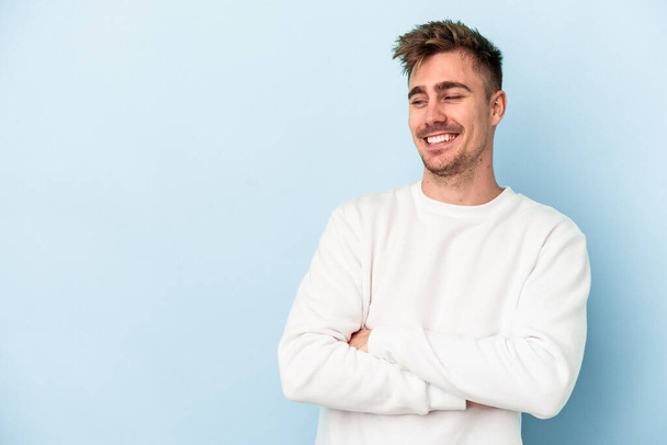 Young caucasian man isolated on blue background smiling confident with crossed arms. - Photo, Image