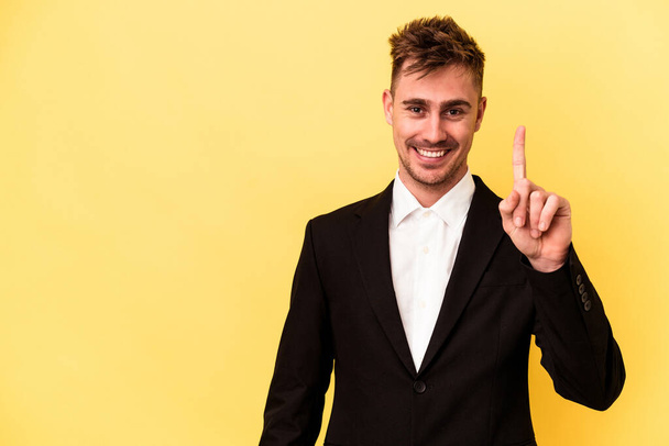Young caucasian business man isolated on yellow background showing number one with finger. - Photo, Image