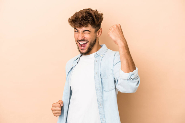 Young arab man isolated on beige background cheering carefree and excited. Victory concept. - Photo, Image
