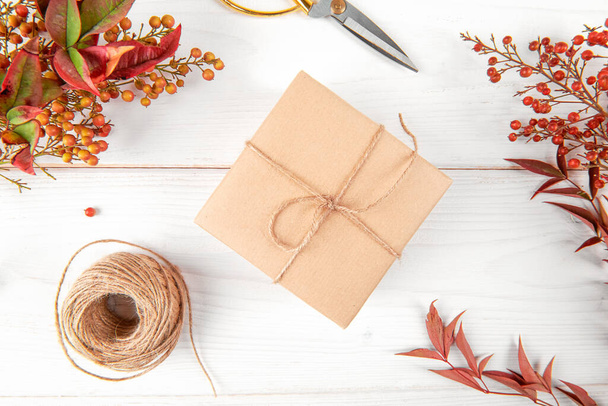 Autumn creative holiday present. Handmade paper gift box with red e orange foliage leaves, on white wooden background. Thanksgiving day, fall background. top view, flat lay - Foto, afbeelding